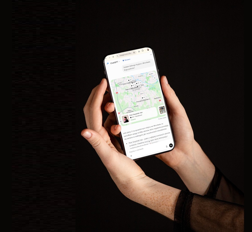 Ręka trzymająca telefon z wynikami ChatGPT pokazującymi widoczność firmy w odpowiedziach AI